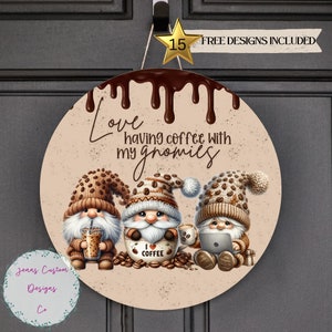 May include: Round wooden sign with a brown background and a dripping chocolate design. The sign features three gnomes wearing brown knit hats and holding coffee cups. The text on the sign reads "Love having coffee with my gnomes".