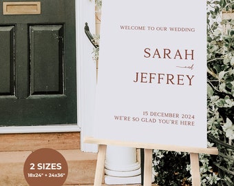 May include: White wedding welcome sign with brown text. The sign says "Welcome to our wedding, Sarah and Jeffrey, 15 December 2024, We're so glad you're here". The sign is on a wooden easel. The sign is available in two sizes: 18x24 inches and 24x36 inches.