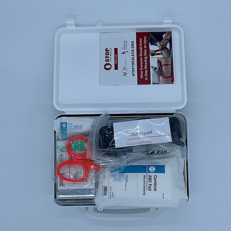 May include: A white first aid kit open to reveal a variety of medical supplies, including a tourniquet, gauze pads, and scissors. The kit is labeled with the text "STOP THE BLEED.ORG" and "ACS".