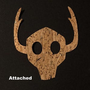 Peut inclure: Deux appliques en forme de crâne en bois, une assemblée et une démontée. L'applique démontée a les bois séparés du crâne. Les textes "Séparé" et "Attaché" sont visibles. Le texte dit aussi "(Vous devrez les aligner avant de les repasser)".