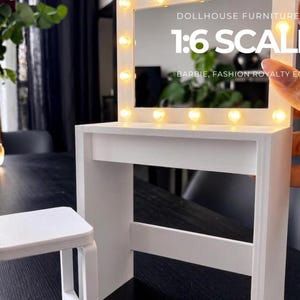 Peut inclure: Un ensemble de coiffeuse pour maison de poupée blanc comprenant un miroir rectangulaire avec des lumières LED chaudes intégrées et une chaise assortie. Le cadre du miroir affiche le texte DOLLHOUSE FURNITURE 1:6 SCALE BARBIE, FASHION ROYALTY ECT...