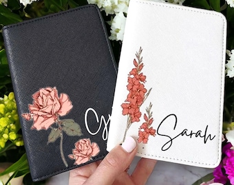May include: Two personalised passport holders with floral designs. One is black with a pink rose and the name "Olivia" and the other is white with a pink flower and the name "Sarah".