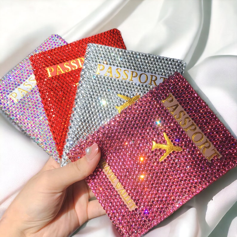 May include: Four passport covers with a sparkly, rhinestone design. The covers are in silver, red, pink, and iridescent. Each cover has the word "PASSPORT" printed in gold lettering.