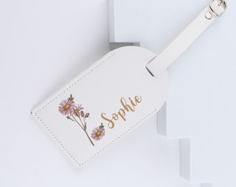 May include: White leather luggage tag with a floral design and the name "Sophie" printed in gold lettering.