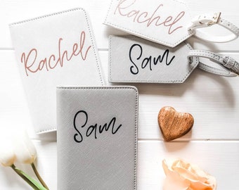 May include: Two passport holders and two luggage tags with the names Rachel and Sam. The passport holders are white and grey, and the luggage tags are white. The luggage tags have a rose gold and black font.