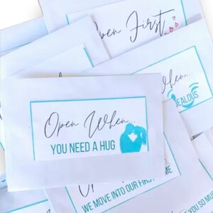 May include: A stack of white envelopes with turquoise borders and text that reads "Open When... You Need A Hug". The envelopes have different messages on them, including "I've Been First" and "Jealous".
