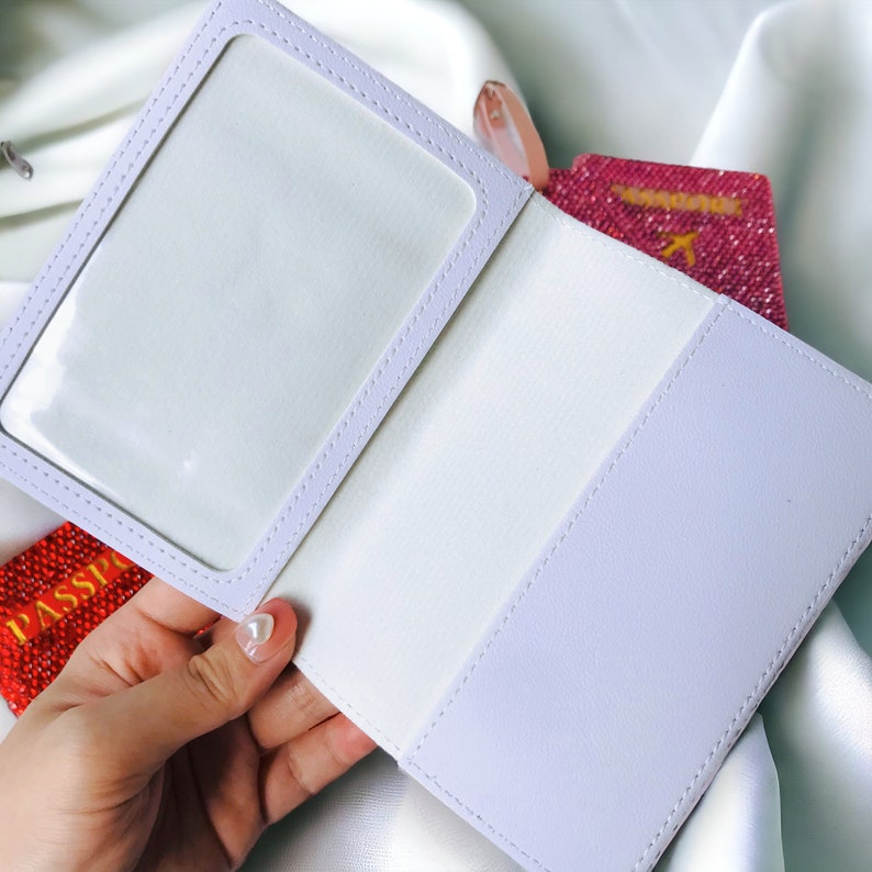 May include: A white passport holder with a clear plastic window for a photo. The holder is open and a red passport with gold glitter is visible inside.