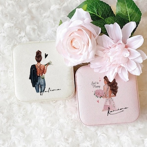 May include: Two white and pink square jewelry boxes with a girl illustration on each. The white box has a girl with a black jacket and the text "Just be Happy" and the pink box has a girl with a pink dress and the text "Just be Happy".