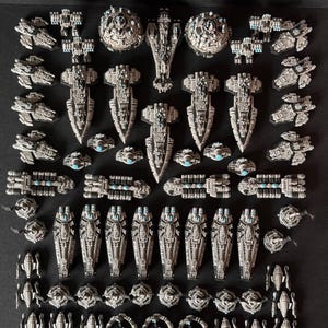 May include: A selection of miniature spaceship models in various designs. The models are mainly grey with blue and silver details. The arrangement includes large, spherical, and elongated ship designs, along with smaller fighter-like crafts.