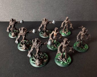 May include: A collection of eight miniature fantasy figures. Each figure is a tree-like humanoid with outstretched arms, holding a gray orb. They stand on green, circular bases with a textured, organic appearance.