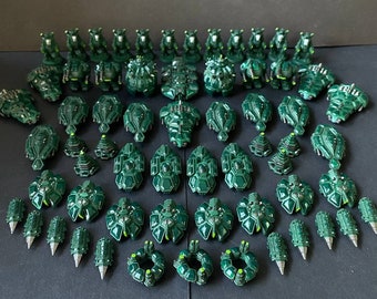 Könnte beinhalten: Eine Sammlung von dunkelgrünen, aus Plastik gefertigten Miniatur-Raumschiffen und anderen Militärfahrzeugen. Die Miniaturen sind in Reihen und Spalten auf einer grauen Oberfläche angeordnet.