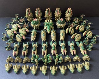 May include: A collection of miniature fantasy creatures in various shapes and sizes. The figures are primarily green and tan with red and pink accents. The assortment includes plant-like and insectoid designs, suitable for tabletop gaming.