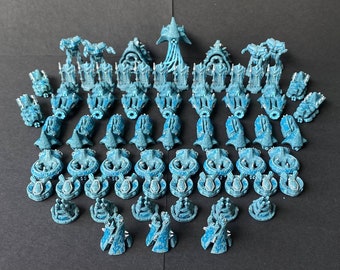 May include: A collection of 3D printed miniature spaceships in various sizes and shapes, painted in a light blue and white color scheme. The miniatures are arranged in a symmetrical pattern on a dark gray surface.