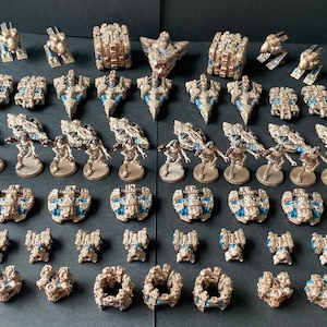 以下が含まれることがあります： 金と青で塗装されたミニチュア宇宙船とフィギュアのコレクション。宇宙船はさまざまなサイズと形があり、フィギュアは円形のベースの上に立っています。