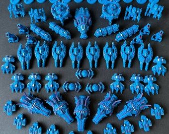 Pode incluir: Uma coleção de naves espaciais em miniatura de plástico azul, algumas com detalhes intrincados, dispostas em filas sobre uma superfície azul escura.