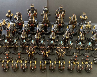 May include: A collection of black and gold miniature spaceships, some with blue accents, arranged in rows on a gray surface.