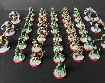 May include: A collection of green and brown painted miniature figures, including orcs, goblins, and trolls, on circular bases. The figures are arranged in rows and columns, with some figures standing and others kneeling.