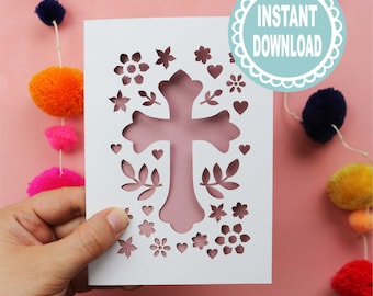 May include: A white card with a cross-shaped cutout, surrounded by floral and heart designs. The card has a pink background visible through the cutouts. The words "INSTANT DOWNLOAD" are in a blue circle. A string of colorful pom-poms hangs in the background.
