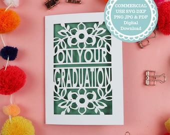 May include: A white card with a green background and a cut-out design of flowers and leaves. The text "On Your Graduation" is cut out of the card.