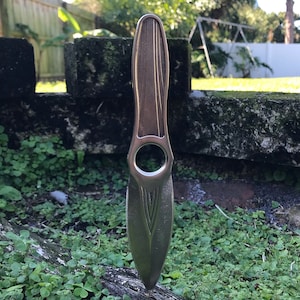 May include: A silver throwing knife with a decorative design on the blade. The knife is pointed and has a hole in the handle.