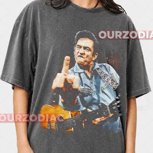 Puede incluir: Camiseta gris oscuro con una imagen desgastada de un hombre tocando la guitarra y mostrando el dedo medio. La imagen es de estilo vintage. El texto "OURZODIA" est&aacute; impreso en la camiseta.