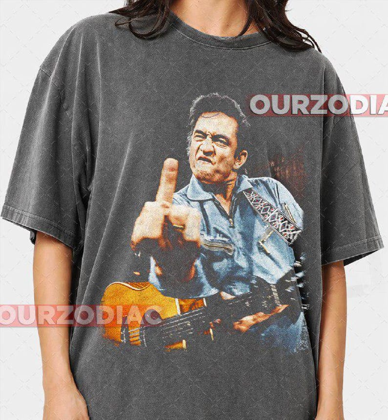 Puede incluir: Camiseta gris oscuro con una imagen desgastada de un hombre tocando la guitarra y mostrando el dedo medio. La imagen es de estilo vintage. El texto "OURZODIA" est&aacute; impreso en la camiseta.