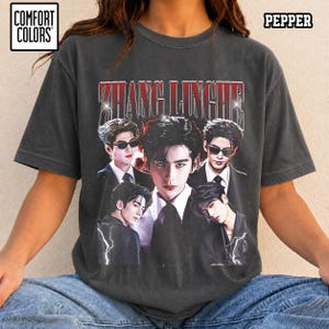 May include: A charcoal gray short-sleeve t-shirt featuring a graphic print of the actor Zhang Linghe in multiple poses. The text ZHANG LINGHE is printed in a bold red font above the images. The shirt includes Comfort Colors and Pepper labels.