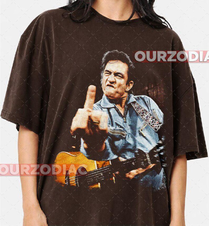 Puede incluir: Camiseta marr&oacute;n con una imagen desgastada de un hombre tocando la guitarra y mostrando el dedo medio. La imagen incluye el texto "OURZODIA". El hombre lleva una camisa vaquera azul.