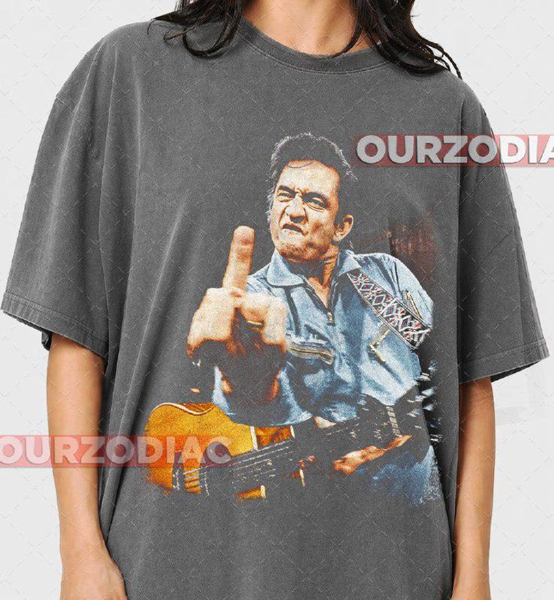 Puede incluir: Camiseta gris oscuro con una imagen desgastada de un hombre tocando la guitarra y mostrando el dedo medio. La imagen es en tonos azules, marrones y naranjas. El texto "OURZODIAC" est&aacute; impreso en la camiseta.