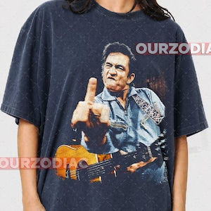 Puede incluir: Camiseta azul marino oscuro con una imagen desgastada de un m&uacute;sico haciendo una peineta mientras sostiene una guitarra. La imagen incluye el texto "OURZODIA" en blanco. El m&uacute;sico lleva una camisa vaquera azul.