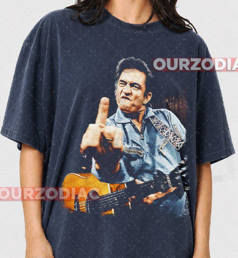 Puede incluir: Camiseta azul marino oscuro con una imagen desgastada de un m&uacute;sico haciendo una peineta mientras sostiene una guitarra. La imagen incluye el texto "OURZODIA" en blanco. El m&uacute;sico lleva una camisa vaquera azul.