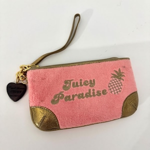 May include: A pink rectangular clutch bag with the words "Juicy Paradise" in gold script and a gold pineapple graphic. The clutch has gold trim, gold corners, and a gold chain with a heart-shaped charm. A brown wrist strap is attached.