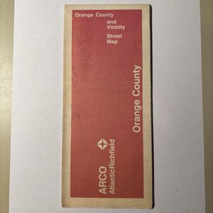 May include: A rectangular folded paper street map of Orange County and Vicinity with a red cover. The text reads Orange County and Vicinity Street Map, Orange County, and the ARCO AtlanticRichfield logo is printed in white at the bottom.