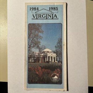 May include: A vintage travel brochure for Virginia, featuring a blue border and the years 1984 and 1985. The brochure displays a photograph of a historic building with white columns and a red-brick facade, surrounded by trees and red tulips.