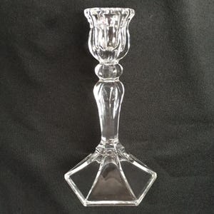 May include: A clear glass candlestick holder with a tulip-shaped top, a rounded center, and a geometric base. The candlestick is approximately 8 inches tall and is designed to hold a single candle.