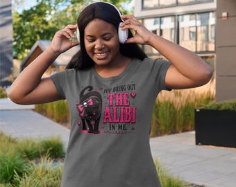 Op de afbeelding: Een antracietgrijs T-shirt met korte mouwen en een afbeelding van een zwarte kat met een roze strik met een schedelaccent. De tekst luidt "YOU BRING OUT THE ALIBI IN ME". Het ontwerp bevat roze hartjes en kleine sterretjes op de voorzijde.