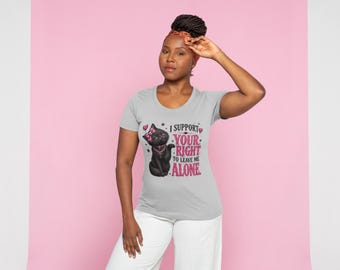 Op de afbeelding: Een lichtgrijs T-shirt met korte mouwen en een afbeelding van een zwarte kat met een roze strik en halsband. De tekst luidt I SUPPORT YOUR RIGHT TO LEAVE ME ALONE in roze en zwarte letters, geaccentueerd met kleine roze hartjes en stippen.
