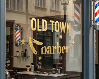 Op de afbeelding: De winkelpui van Old Town Barber Shop heeft een donkergrijs frame, een glazen raam met gouden letters, een afbeelding van een scheermes en twee rood-wit-blauwe kapperspalen. Binnen staat een bruine leren kappersstoel bij een houten balie.