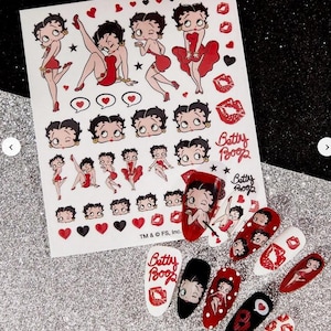 May include: A sheet of Betty Boop nail art transfers and several decorated nails. The transfers feature various poses of Betty Boop, hearts, and lips. The nails are painted with Betty Boop designs, red, black, and white.