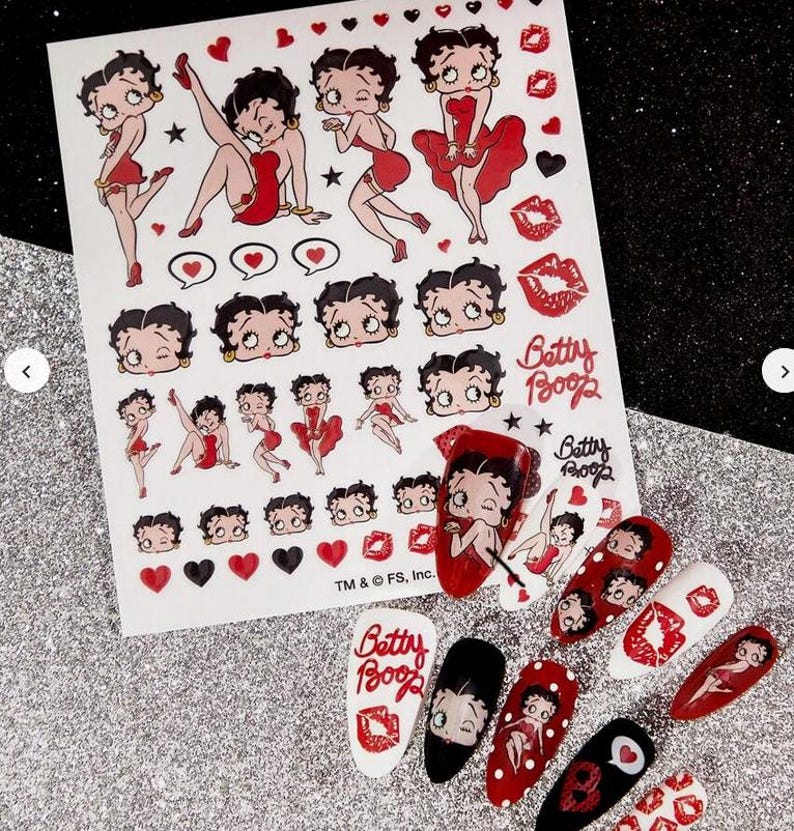 May include: A sheet of Betty Boop nail art transfers and several decorated nails. The transfers feature various poses of Betty Boop, hearts, and lips. The nails are painted with Betty Boop designs, red, black, and white.