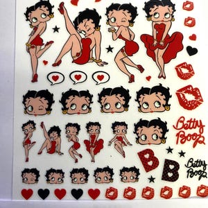 May include: A sheet of Betty Boop stickers. The stickers feature the cartoon character in various poses, all wearing a red dress. There are also hearts, stars, and the words "Betty Boop" in a cursive font. The background is white.