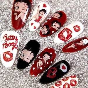 May include: A selection of artificial nails decorated with Betty Boop designs. The nails display Betty Boop in red, black, and white, with polka dots, hearts, and the text "Betty Boop".