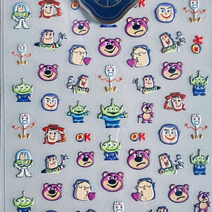 May include: A sheet of colorful nail art stickers featuring characters from the Toy Story franchise. The stickers include Woody, Buzz Lightyear, Jessie, Rex, and Mr. Potato Head. The stickers are arranged in a grid pattern on a white background. The text "TS-1163 玩具乐园 浮雕 TENSOR" is printed at the bottom of the sheet.