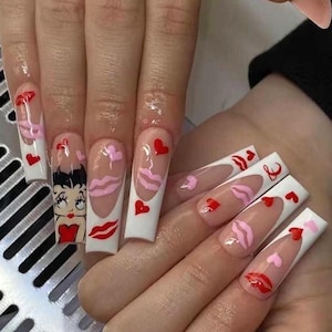 May include: Long, square acrylic nails with a Valentine's Day theme. Designs include red hearts, pink lips, and a Betty Boop cartoon. The nails have a white border and a clear base.