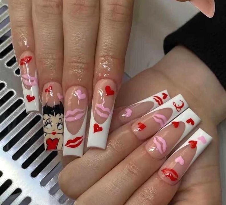 May include: Long, square acrylic nails with a Valentine's Day theme. Designs include red hearts, pink lips, and a Betty Boop cartoon. The nails have a white border and a clear base.
