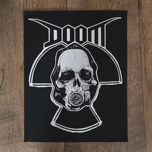 May include: Black patch featuring a white skull wearing a gas mask, with the word "DOOM" above. The design is a detailed illustration, perfect for jackets, bags, or other accessories. The patch is rectangular.