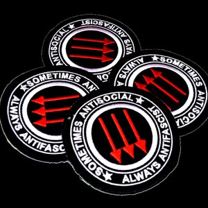 May include: Four black and white circular patches with red arrows pointing to the right. The patches have the text "Always Anti-Fascist" and "Sometimes Antisocial" around the edge.
