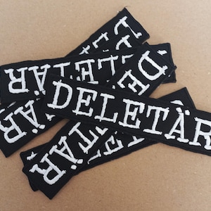 Könnte beinhalten: Ein Stapel schwarzer Stoffpatches mit weiß gestickten Buchstaben, die "DELETAR" lesen.