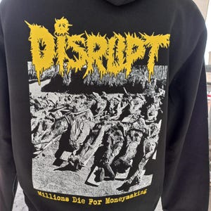Könnte beinhalten: Schwarzer Kapuzenpullover mit einem gelben Grafikdruck des Wortes "DISRUPT" und dem Text "Millions Die For Moneymaking".