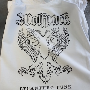 Könnte beinhalten: Weißes T-Shirt mit einem schwarzen Grafikdesign eines zweiköpfigen Wolfes mit Flügeln und dem Text "Wolfpack" darüber und "Lycanthro Punk" darunter.